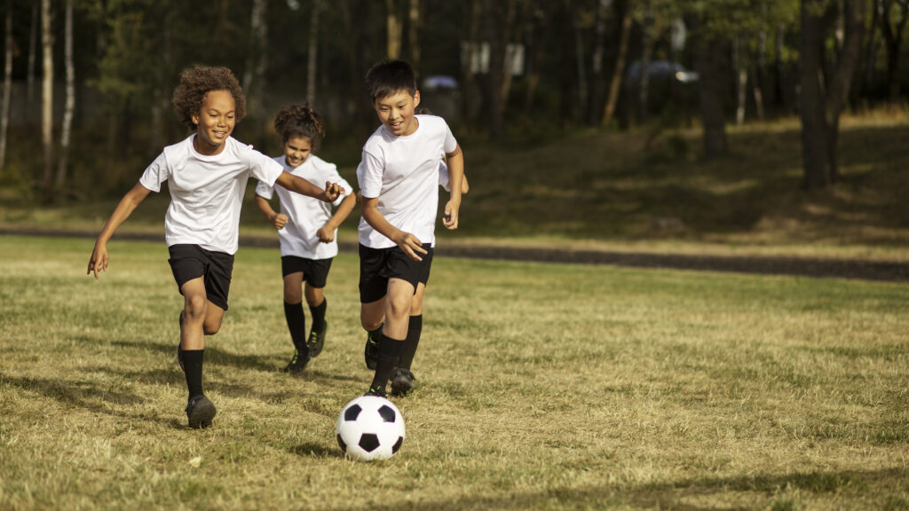 Crianças jogando futebol em um campo gramado ao ar livre, ilustrando o campo de futebol do Solares Residencial & Clube em Capivari (SP). A imagem destaca a estrutura de esporte, lazer e bem-estar do condomínio fechado planejado pela Forner Empreendimentos (imagem meramente ilustrativa). Uma excelente oportunidade para famílias que buscam comprar terrenos e lotes residenciais prontos para construir na região de Capivari e em cidades vizinhas como Rafard, Mombuca, Elias Fausto, Monte Mor, Porto Feliz, Rio das Pedras e Santa Bárbara d'Oeste.